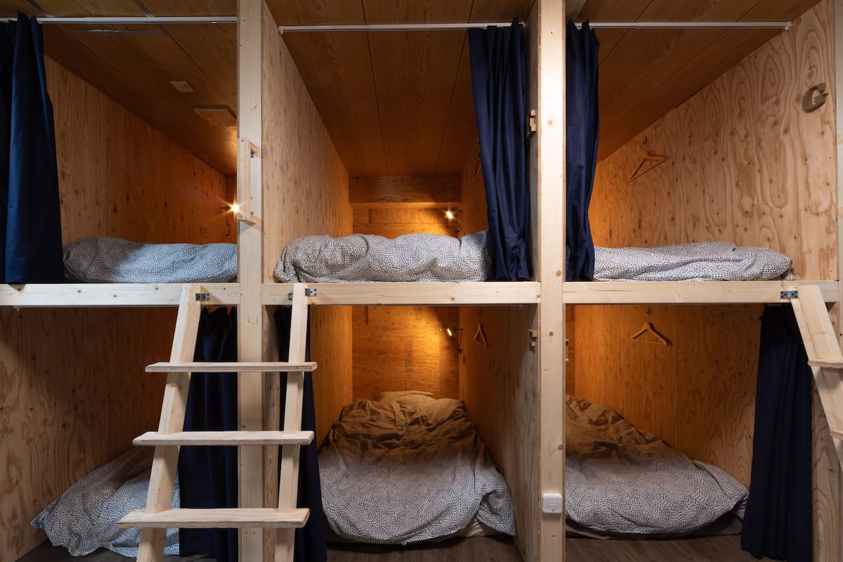 Een slaapkamer met een houten stapelbed, een ladder, gordijnen en een hanglamp.