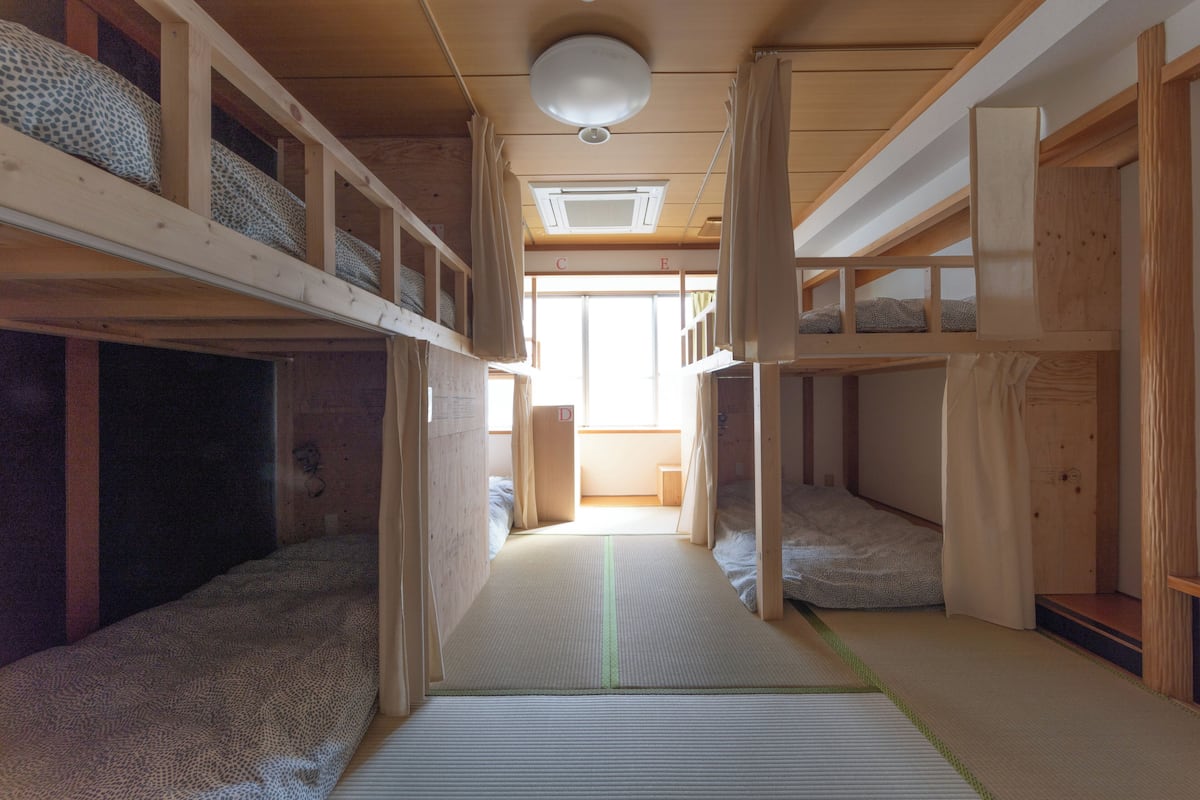 Een traditionele Japanse kamer met tatami vloeren, houten stapelbedden en een schuifdeur naar een lichte ruimte.