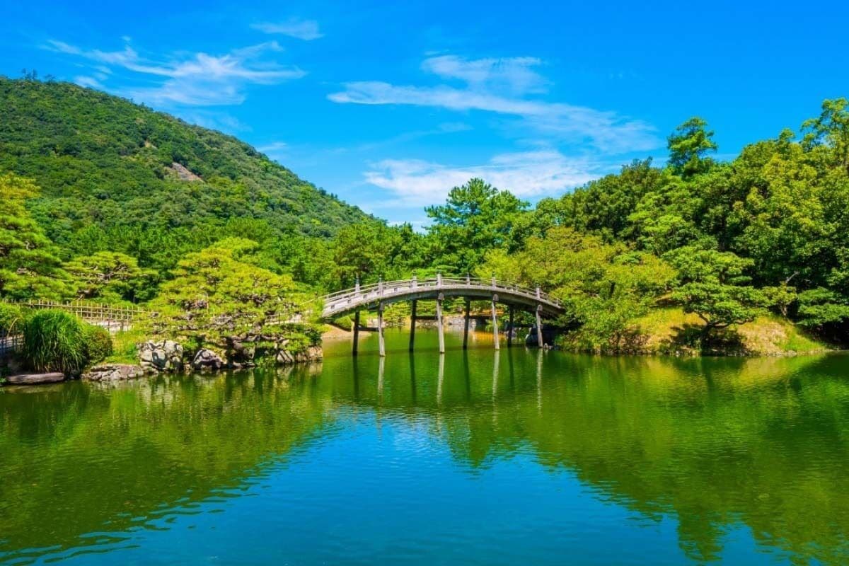 A serene landscape with a wooden bridge over a calm lake, surrounded by lush greenery and hills.