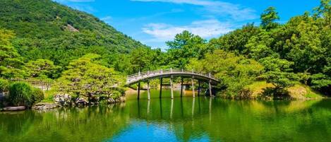 A serene landscape with a wooden bridge over a calm lake, surrounded by lush greenery and hills.