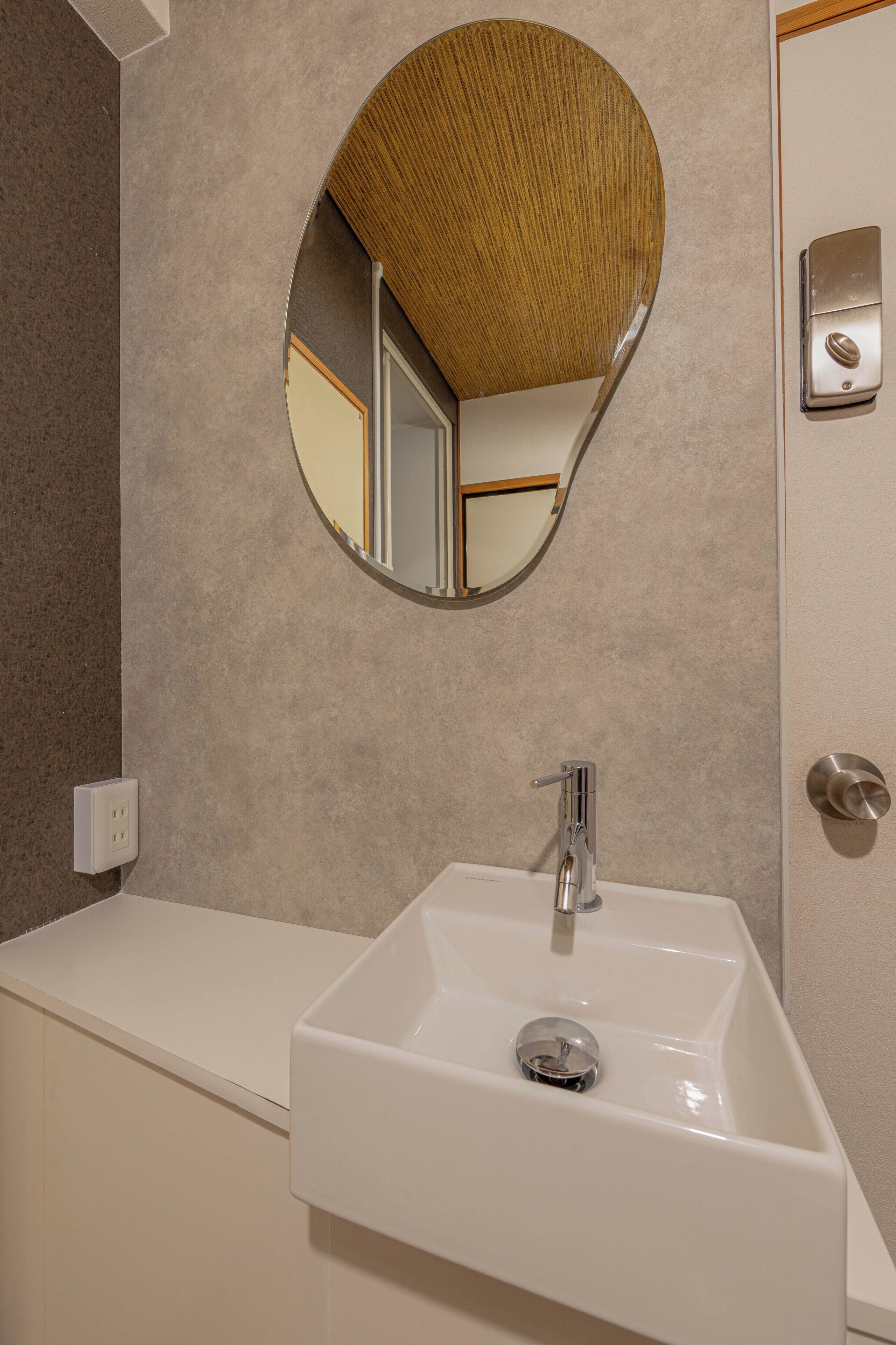 A bathroom with a white sink, a round mirror, and a wooden ceiling.