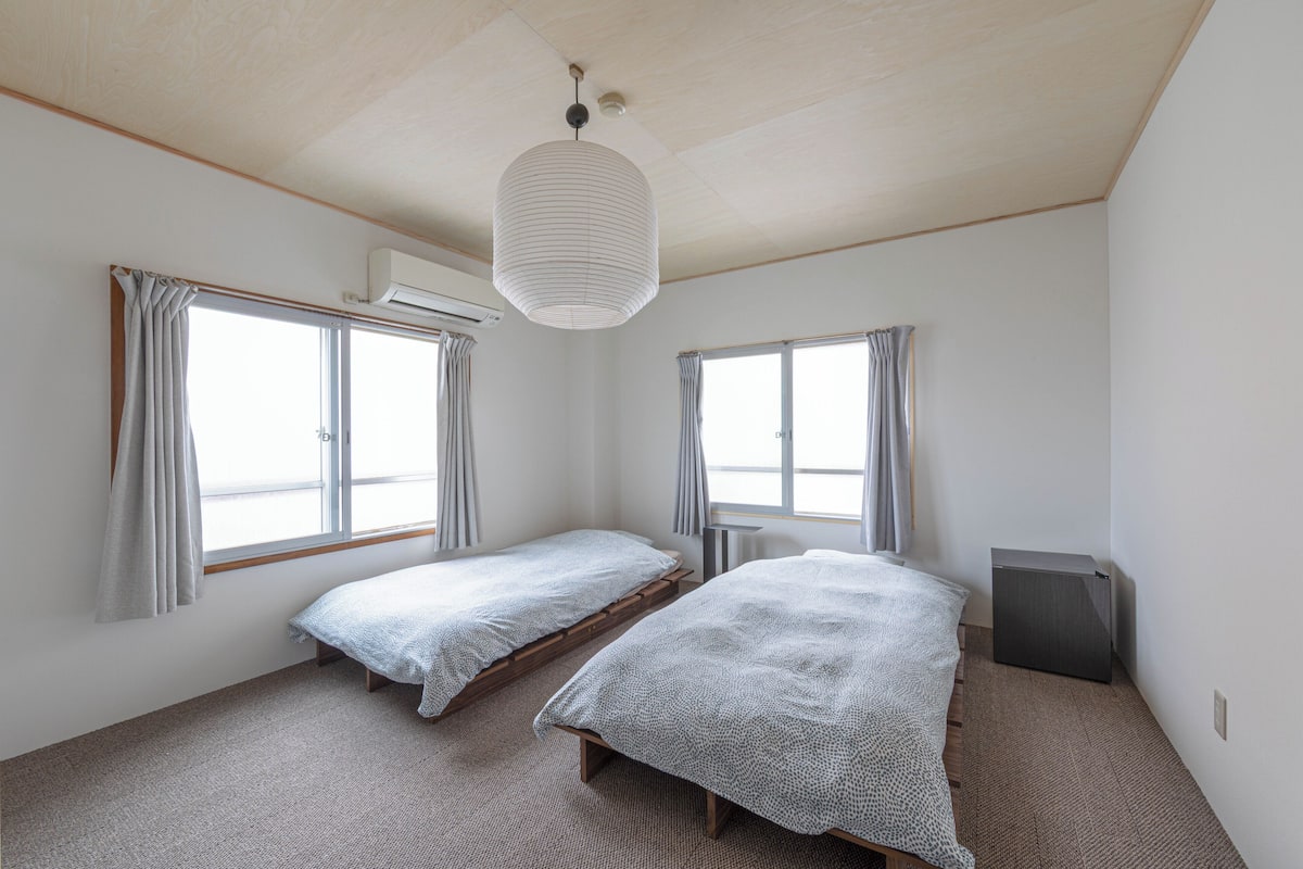 Een slaapkamer met twee eenpersoonsbedden, een plafondlamp en een raam met gordijnen.