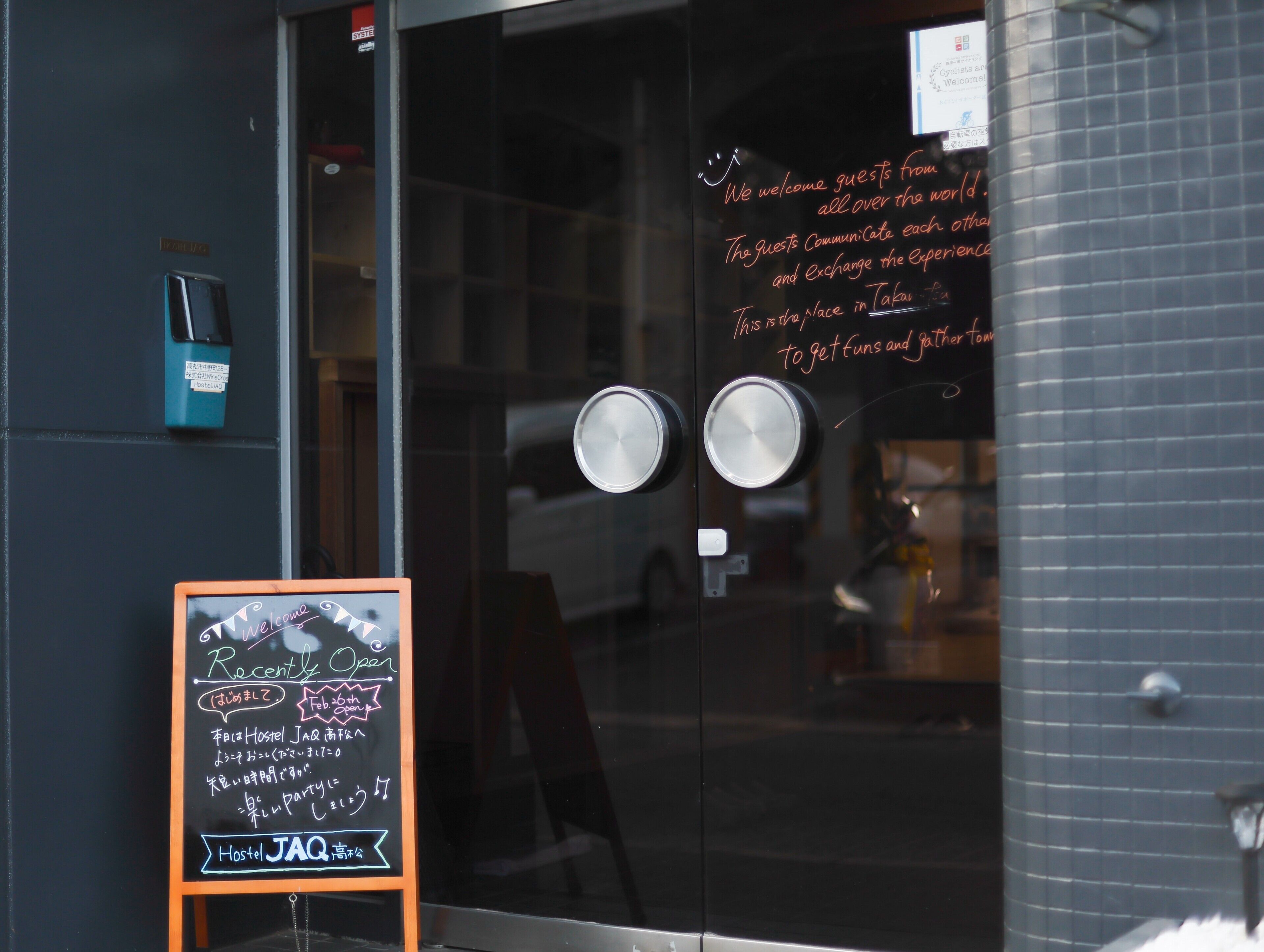 A hostel entrance with a chalkboard sign indicating recent openings and a welcome message.
