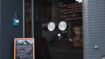 A hostel entrance with a chalkboard sign indicating recent openings and a welcome message.