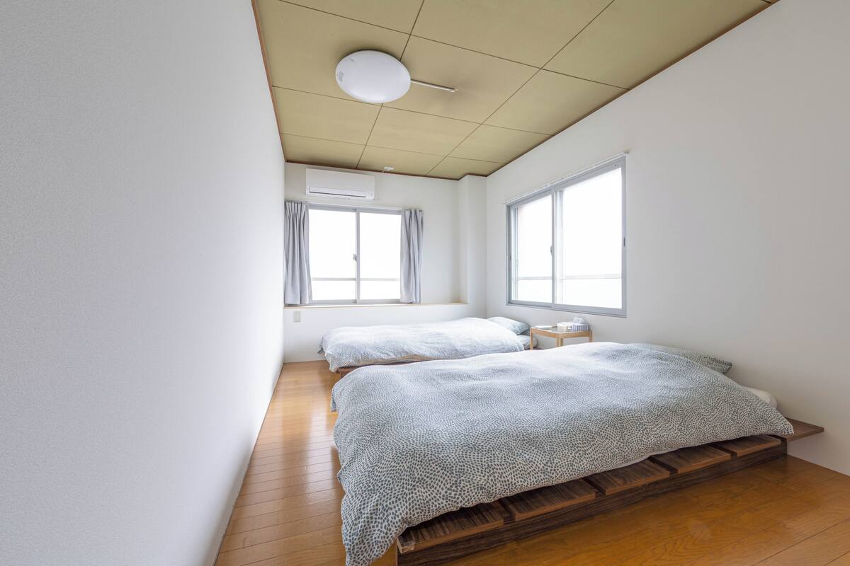 Een slaapkamer met twee bedden, een plafondventilator en grote ramen.