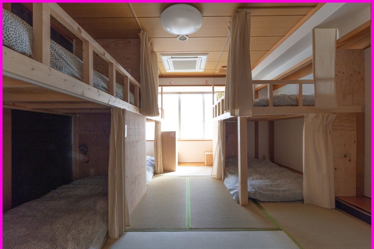 Une chambre avec des lits superposés, un couloir central, des murs en bois et un ventilateur de plafond.