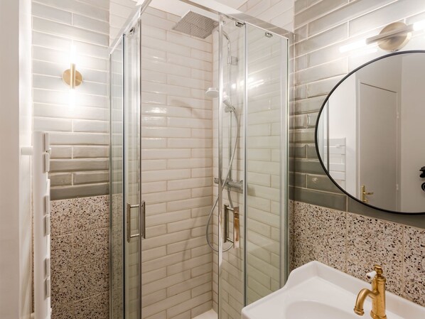 A modern bathroom with a glass-enclosed shower, a white sink with a gold faucet, and a large mirror.
