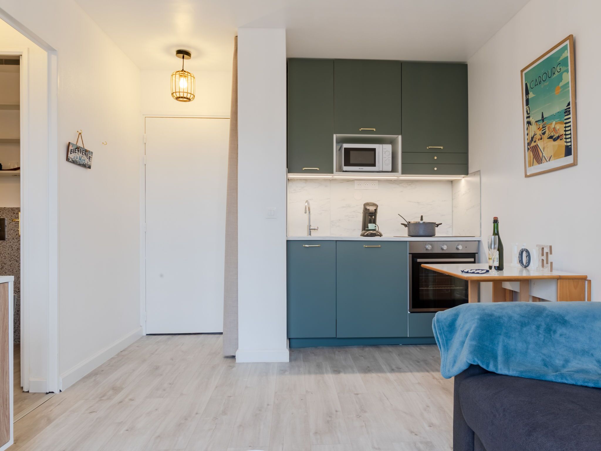 Een compacte keuken met blauwgroene kastjes, een magnetron, een koffiezetapparaat en een kleine oven.