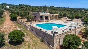 A stone pool with lounge chairs, a small building with a roof, and a path leading to a white building in a rural setting. - 1159 Perla Bianca by Perle di Puglia (Ugento)