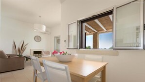 A modern living room with a dining table, white chairs, a sofa, a large window with a view, and a clock on the wall. - 1159 Perla Bianca by Perle di Puglia (Ugento)