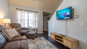A living room with a sofa, ottoman, and a flat-screen TV mounted on the wall.