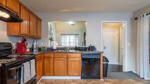 A modern kitchen with wooden cabinets, a black stove, a dishwasher, and a large island with a sink.