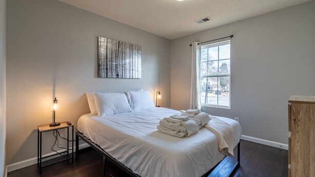A bedroom with a bed, bedside lamps, a window, and a painting on the wall.