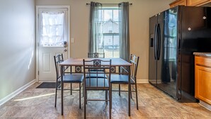 A kitchen with a dining table, chairs, a refrigerator, and a window with curtains.