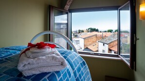A hotel room with a bed, a window, and a view of buildings outside.