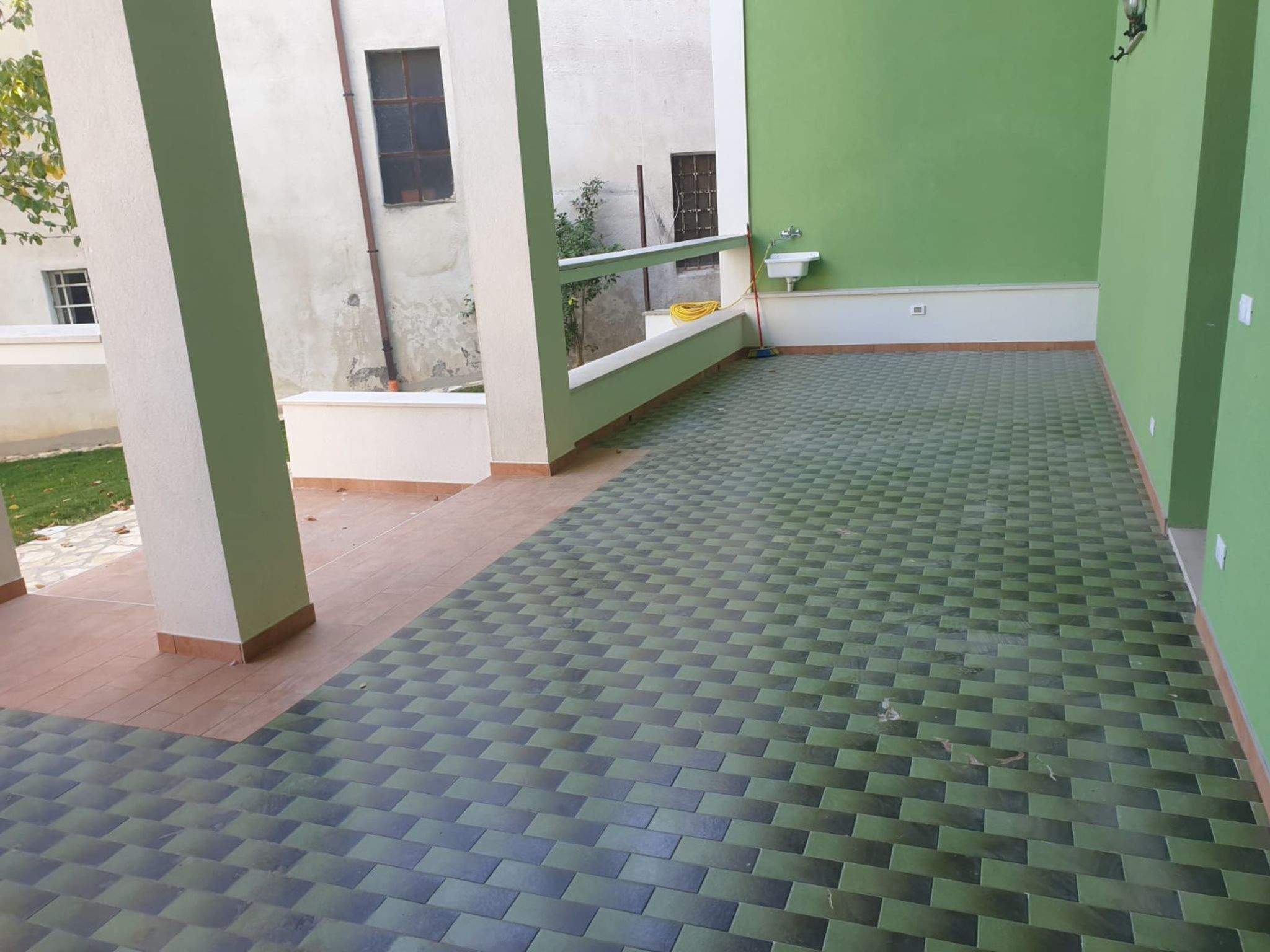 A covered outdoor area with a tiled floor, a bench, and a sink.