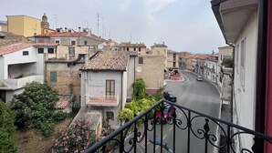 A residential area with terracotta-tiled roofs, a winding street, and a balcony with a metal railing.