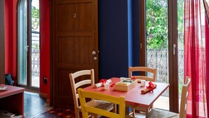 A room with a wooden door, a red table with chairs, and a view of greenery outside.