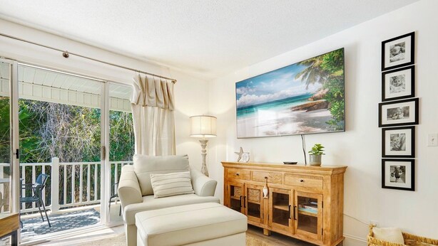 Ein Zimmer mit Balkon, einer Couch, einem Holzschrank und einem Strandbild.