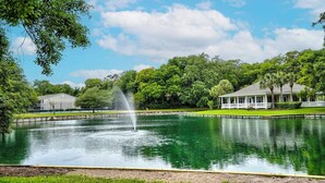 Ein friedlicher Park mit einem Brunnen, ein weißes Gebäude mit einer Veranda und üppigem Grün.