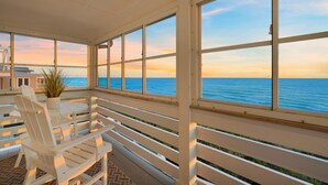 A covered outdoor seating area with white chairs and a potted plant, overlooking the ocean. - PELICAN PLACE: Gulf Front 75ft Private Beach! Pool + Hot Tub! Elevator, Outdoor Kitchen, Green Egg (Inlet Beach)