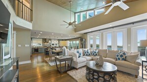 A spacious living area with a high ceiling, large windows, and a modern kitchen in the background. - PELICAN PLACE: Gulf Front 75ft Private Beach! Pool + Hot Tub! Elevator, Outdoor Kitchen, Green Egg (Inlet Beach)