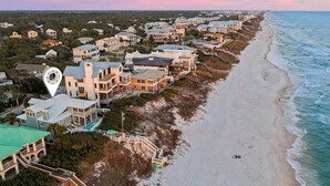 An aerial view of a coastal residential area with houses, a beach, and a lifeguard tower. - PELICAN PLACE: Gulf Front 75ft Private Beach! Pool + Hot Tub! Elevator, Outdoor Kitchen, Green Egg (Inlet Beach)