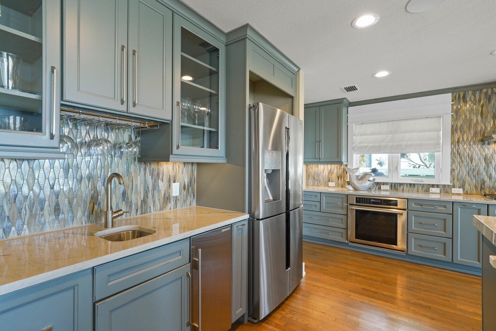 Una cocina moderna con armarios azul claro, un refrigerador de acero inoxidable y un horno empotrado.