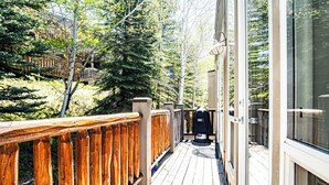 A wooden deck with a metal railing, a barbecue grill, and a glass door leading to a building.