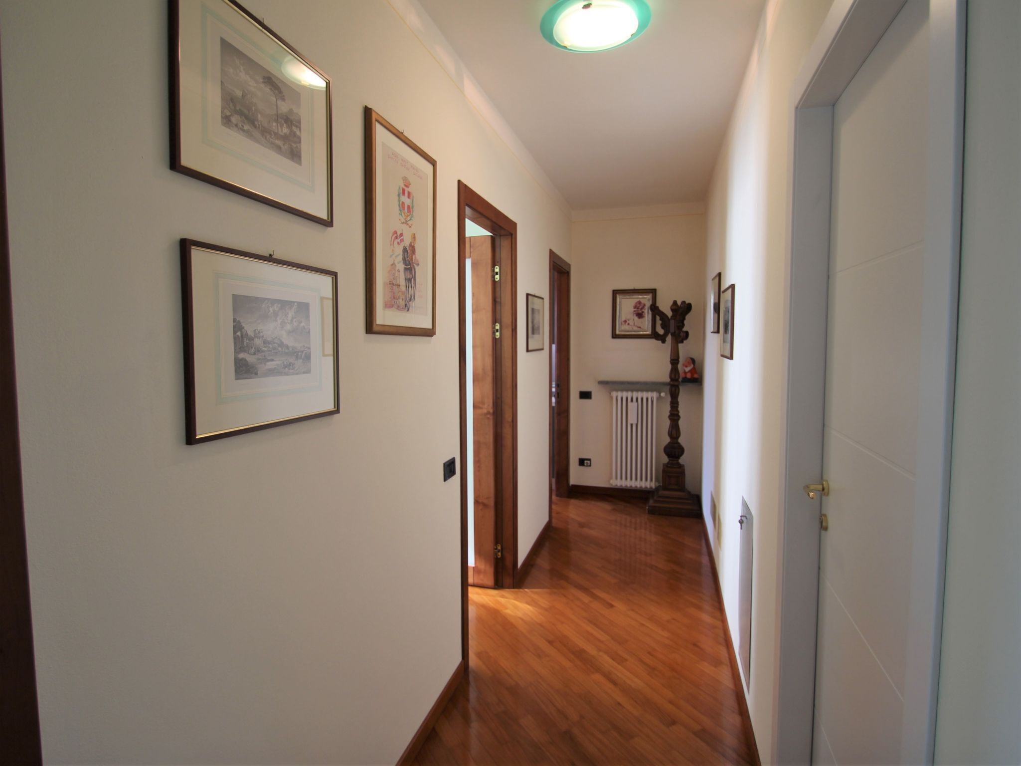 A hallway with framed pictures on the walls, a radiator, and a wooden floor.