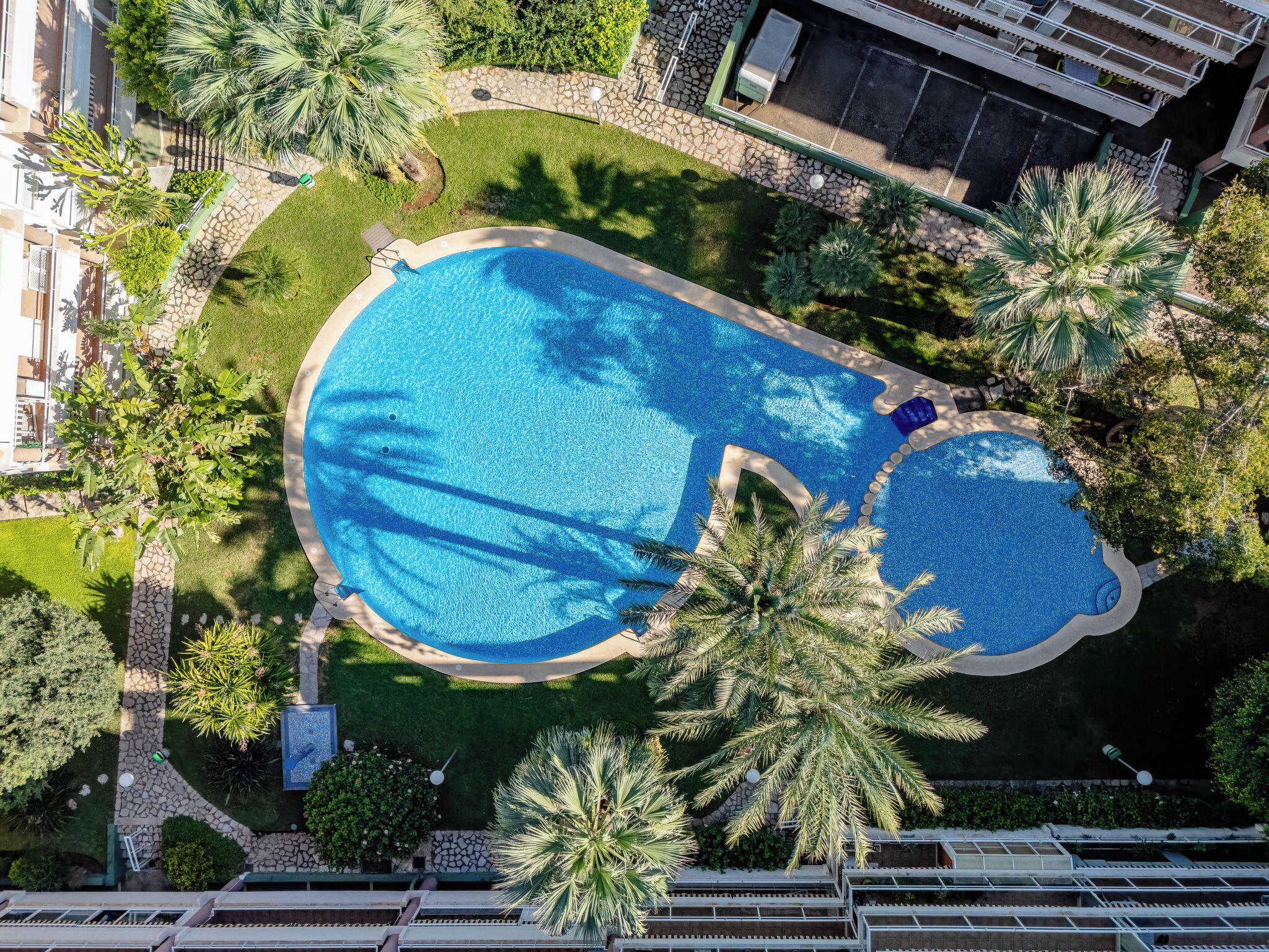 Vista aérea de um resort com uma grande piscina cercada por palmeiras e um caminho de pedra.