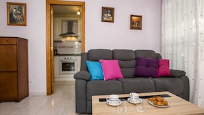 A living room with a grey sofa, a wooden coffee table with cups and pastries, a kitchen in the background, and a door leading to another room. - Dianium by Interhome (Dénia)