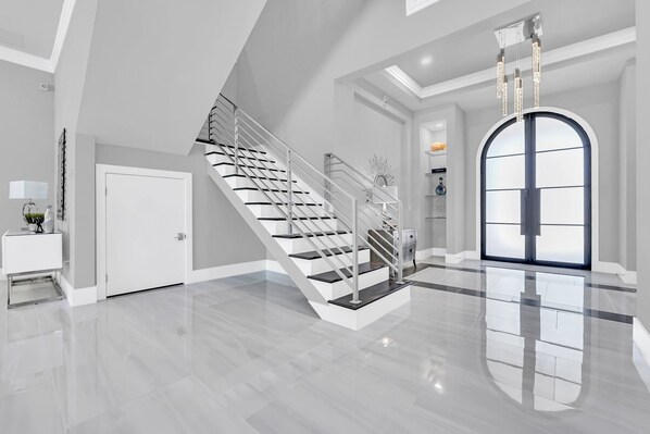 A spacious, modern interior with a polished staircase, a large arched doorway, and a minimalist design.