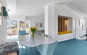 A modern interior with a central white table, grey chairs, a blue carpet, and a wooden bench with a yellow cushion. - Amazing home in Grenaa with kitchen (Grenaa)