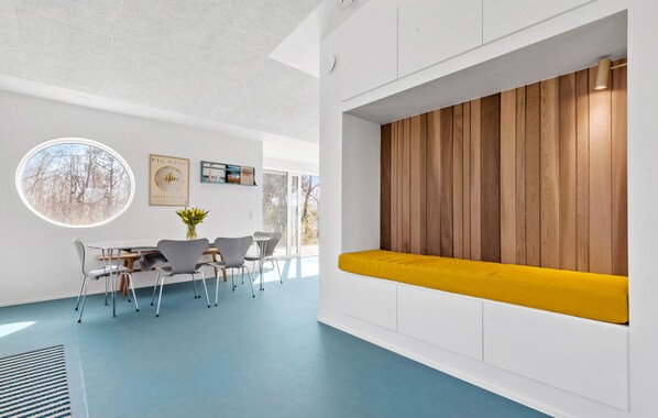 Un interior moderno con suelo azul, un ventanal redondo, pared de paneles de madera y un banco amarillo.
