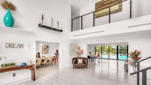 A spacious living area with a dining table, a sofa, and a staircase leading to a balcony.