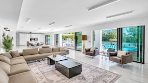 A modern living room with a sectional sofa, a coffee table, and a view of a swimming pool through large windows.