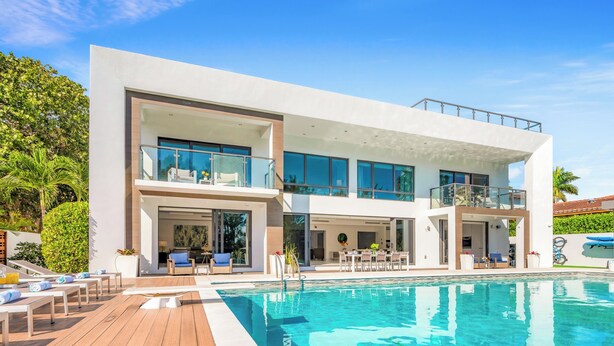 A modern two-story house with a swimming pool, outdoor seating, and a balcony.