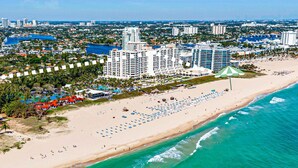 A coastal cityscape with a beachfront featuring numerous beach umbrellas and a large hotel with multiple stories.