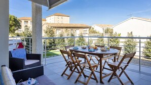 A balcony with a table set for dining, outdoor furniture, and a view of surrounding buildings.