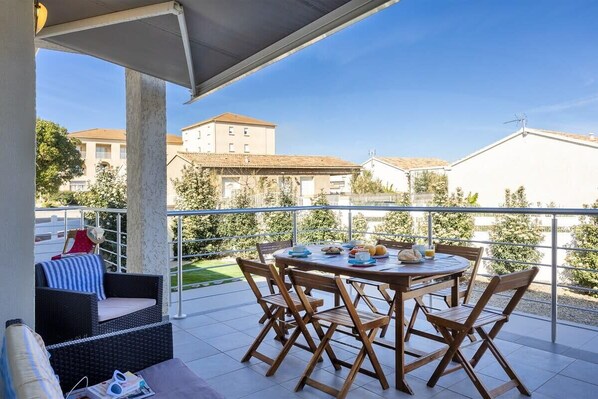 A balcony with a table set for dining, outdoor furniture, and a view of surrounding buildings.