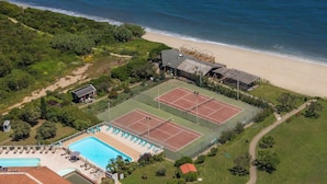 An aerial view of a coastal property with a tennis court, pool, and beach access.