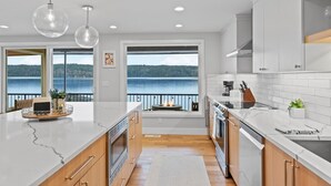 A modern kitchen with a large island, wooden cabinets, and a view of the lake.