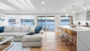 A modern living room with a large sofa, a dining area with bar stools, and a kitchen with a large island.