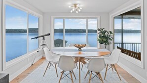A dining area with a large table, white chairs, and a view of a lake.