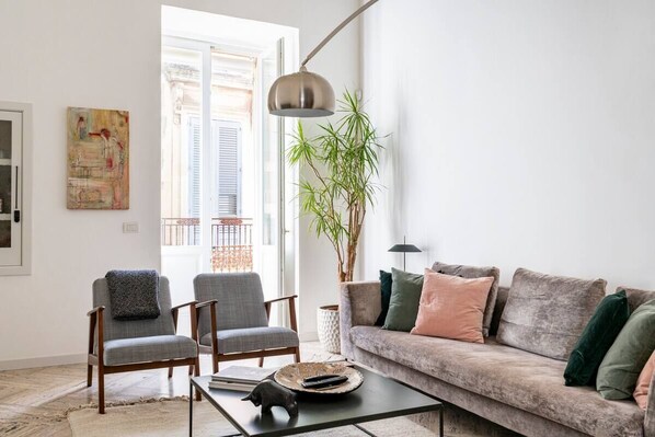 Een woonkamer met een bank, twee fauteuils, een salontafel en een grote plant.