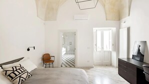 Quarto com cama, cadeira, penteadeira e porta para outro cômodo.