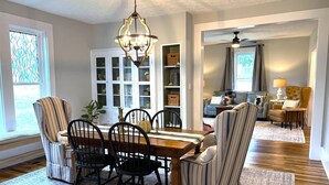 A dining area with a wooden table and chairs, a chandelier, and a view of a living room with a sofa and a lamp.