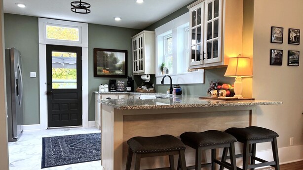 A kitchen with a marble countertop, dark wooden stools, and a black door.