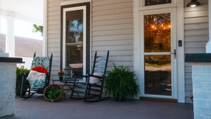 A porch with two rocking chairs, a basket, and potted plants.